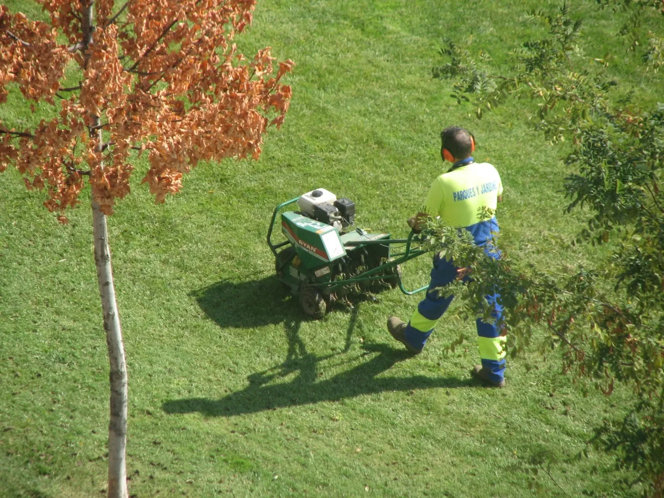 A Green Scene crewman running a core aerator across a sloped lawn beside a house