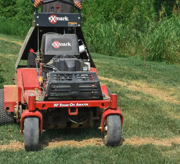 A walk-behind core aerator parked on a lawn with soil plugs lying behind it