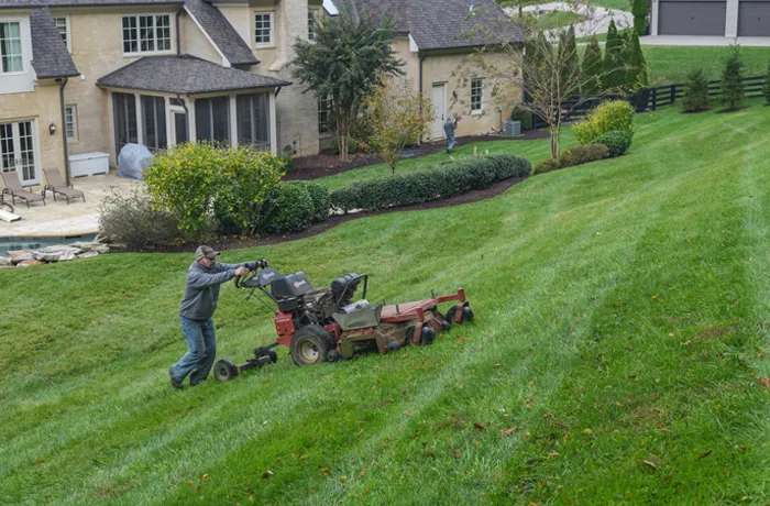 A Green Scene crewman mowing across a steep sloped front yard below a house
