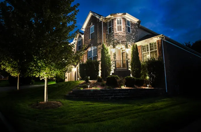 A two-story brick and stone home in Nolensville at night, with uplit trees in the front lawn, small path lights along a stacked-block retaining wall and a lit front porch
