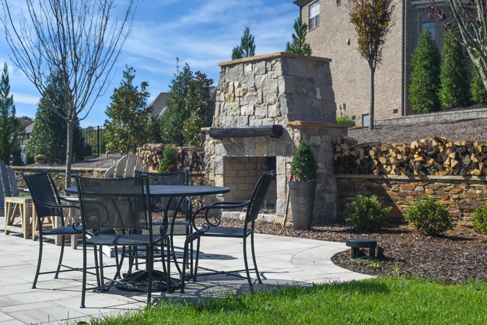 A paver patio with a dining set beside a stacked-stone outdoor fireplace