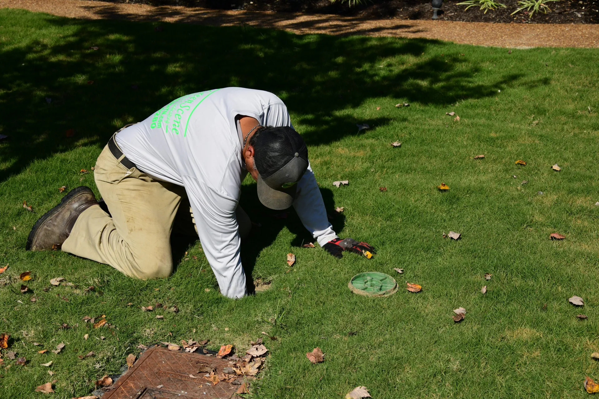 A Green Scene technician kneeling in a front lawn beside a round green irrigation box lid