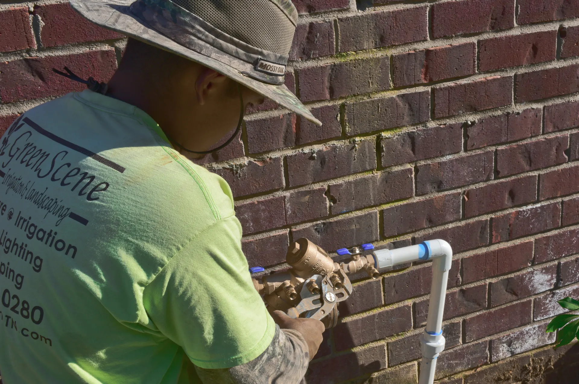 A Green Scene technician working on a brass backflow assembly mounted on a brick wall