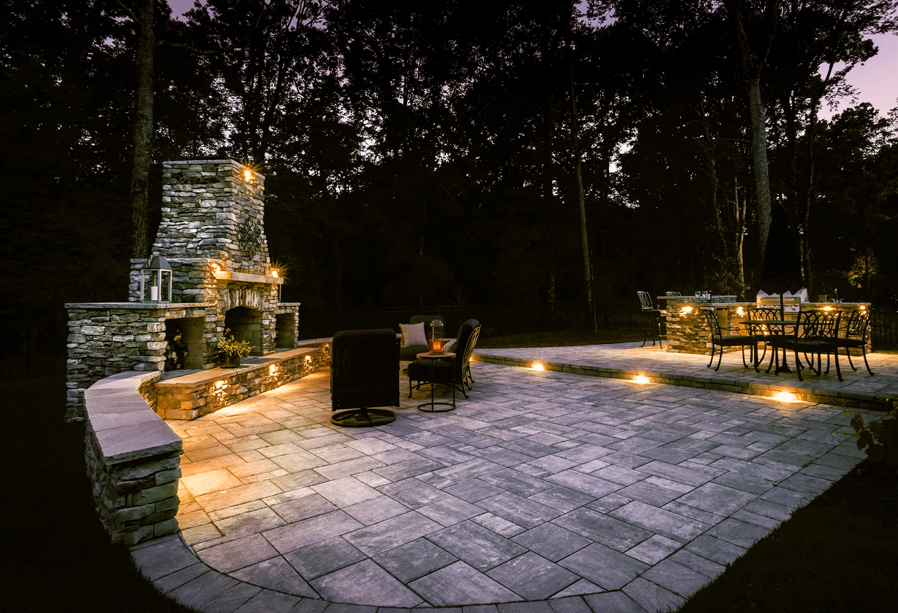 A stacked-stone fireplace and paver patio lit at night