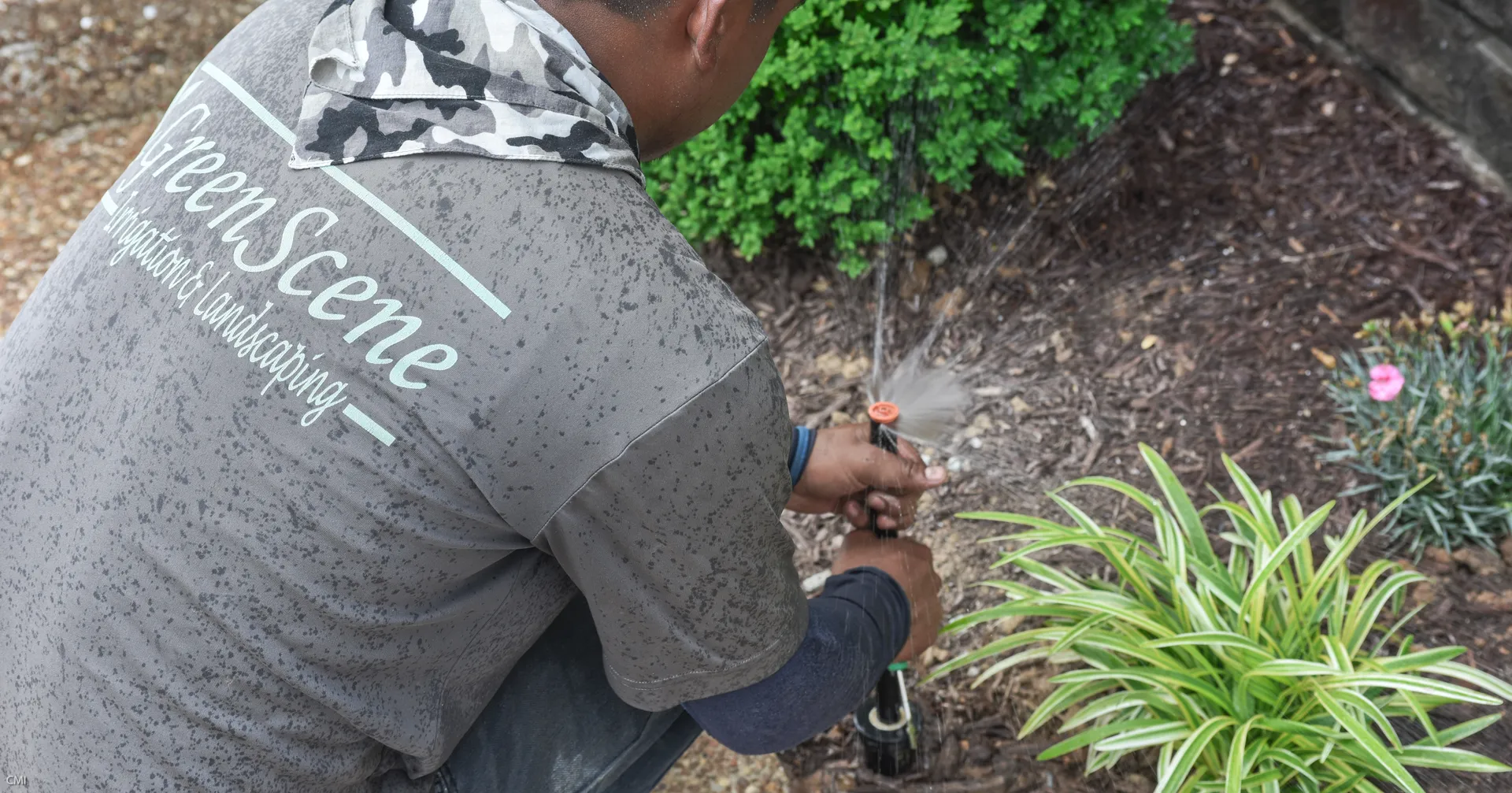 A Green Scene technician adjusting a spray head in a mulched planting bed