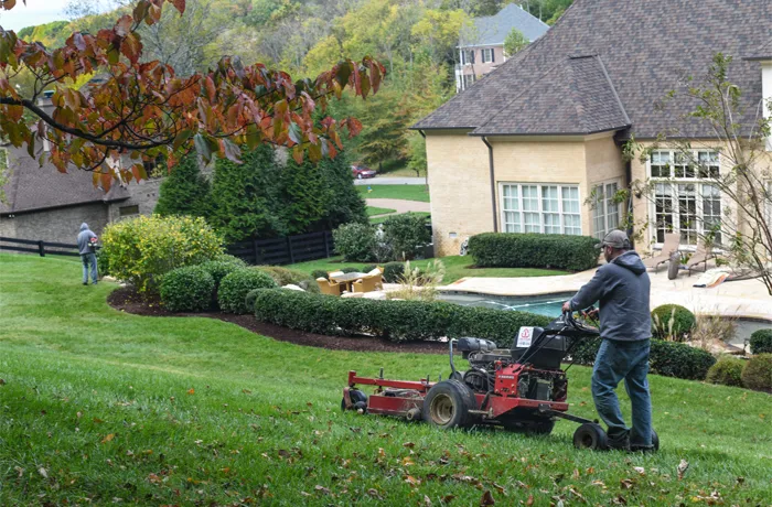Two Green Scene crewmen mowing a front lawn with walk-behind and riding mowers