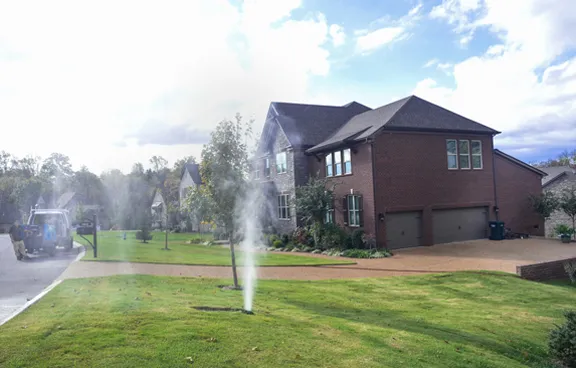 A rotor head spraying during a zone test on the front lawn of a large brick house